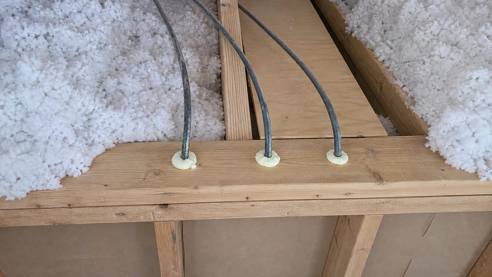 Three cables rising through an attic top plate with neat foam seals around each hole