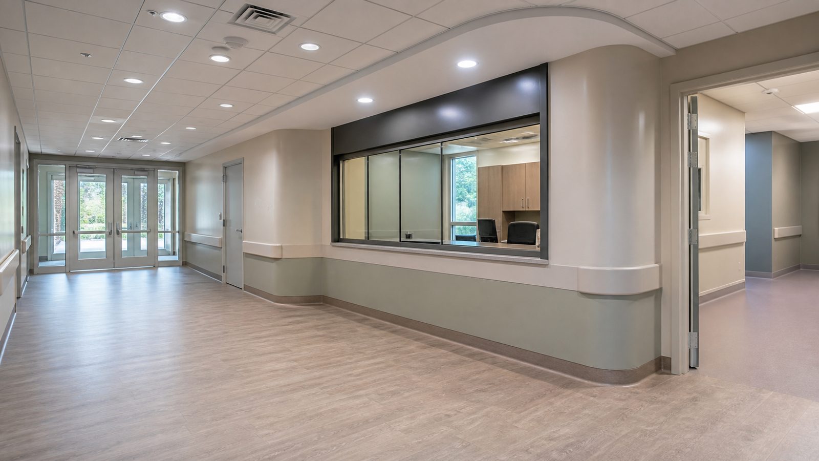 Empty behavioral health observation corridor with durable finishes, protected glazing, and controlled room entry