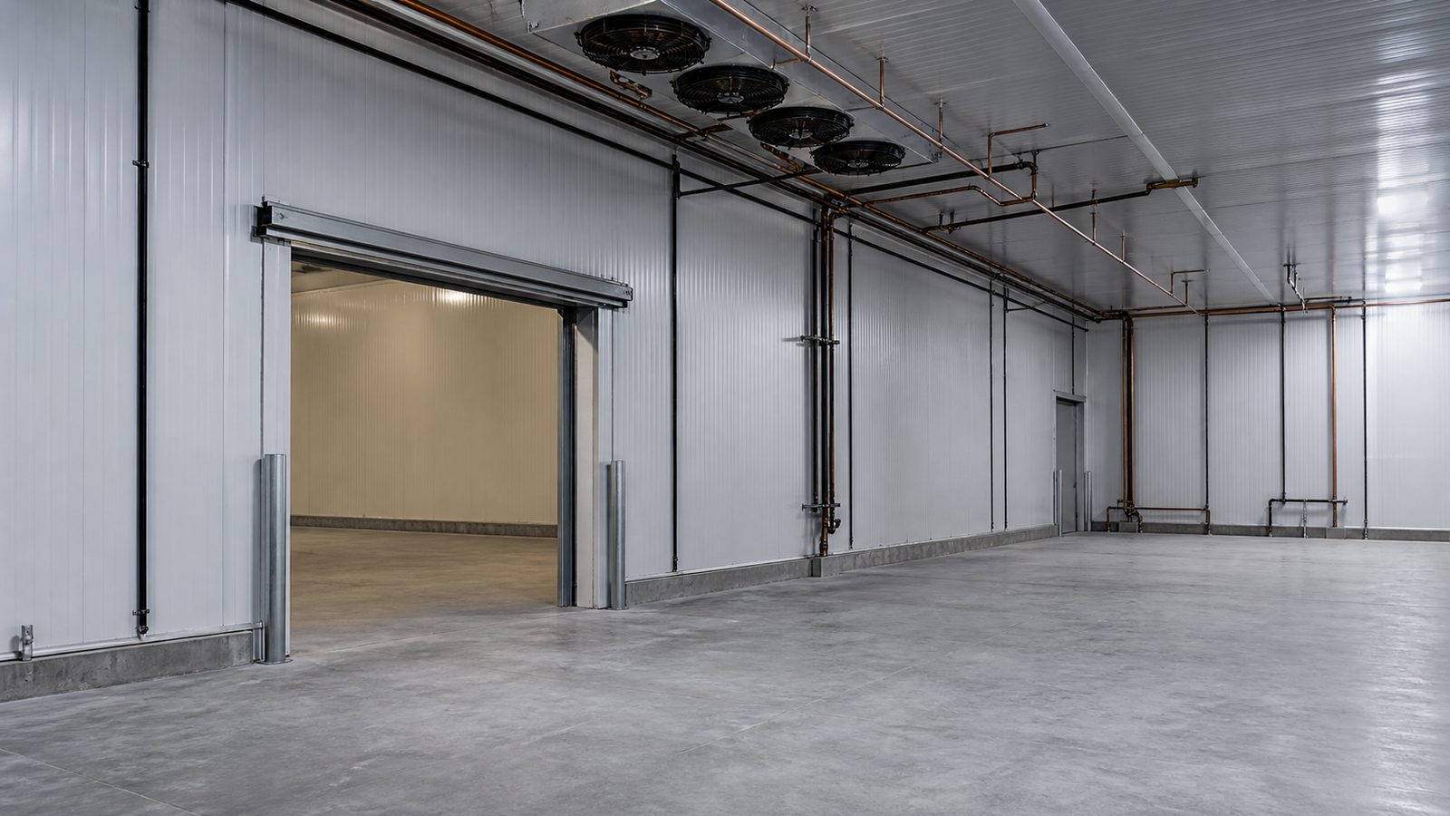 Empty commercial cold-storage room with insulated metal wall panels, sealed joints, refrigeration lines, and insulated doorway