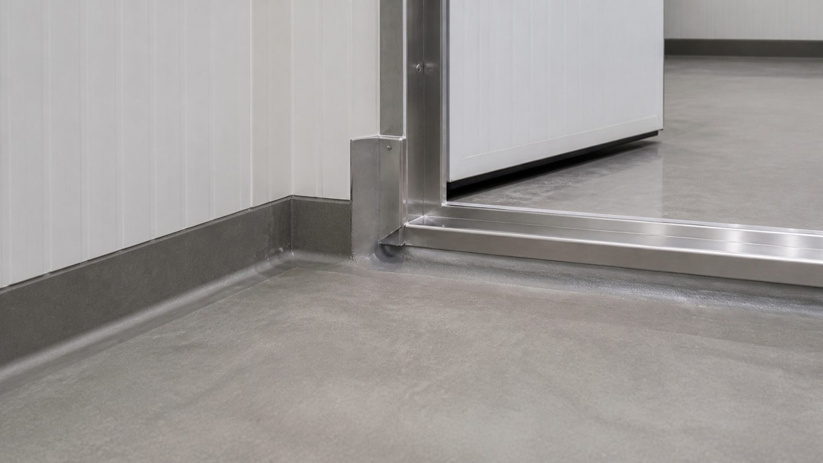 Insulated cold-storage door threshold with sealed panel base, protective curb detail, and smooth floor transition