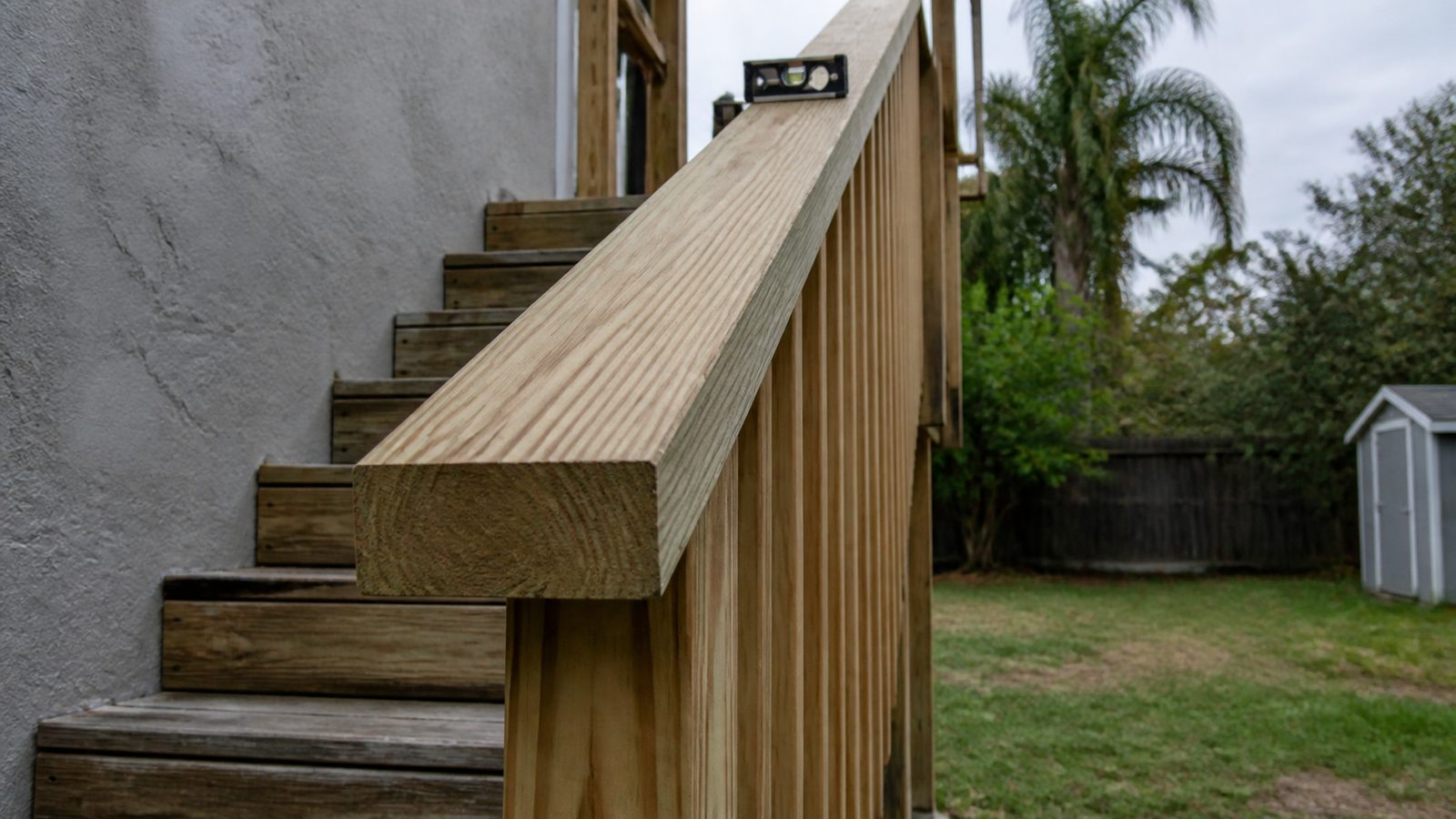 Wide flat wood board serving as the gripping rail on exterior deck stairs