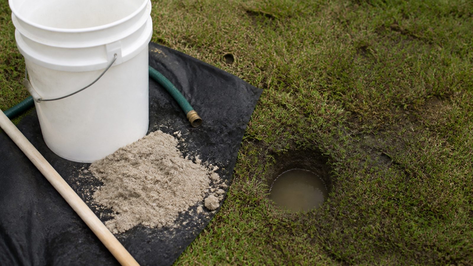 Small water-filled percolation test bore beside a bucket and soil tarp