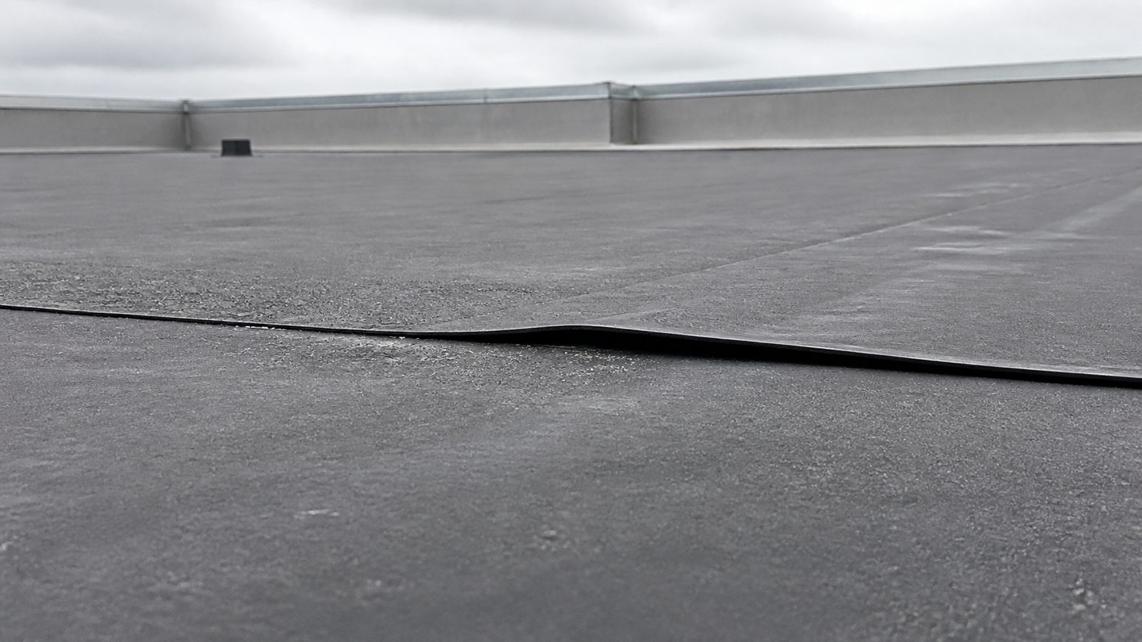 Lifted edge along a weathered black EPDM roof lap seam
