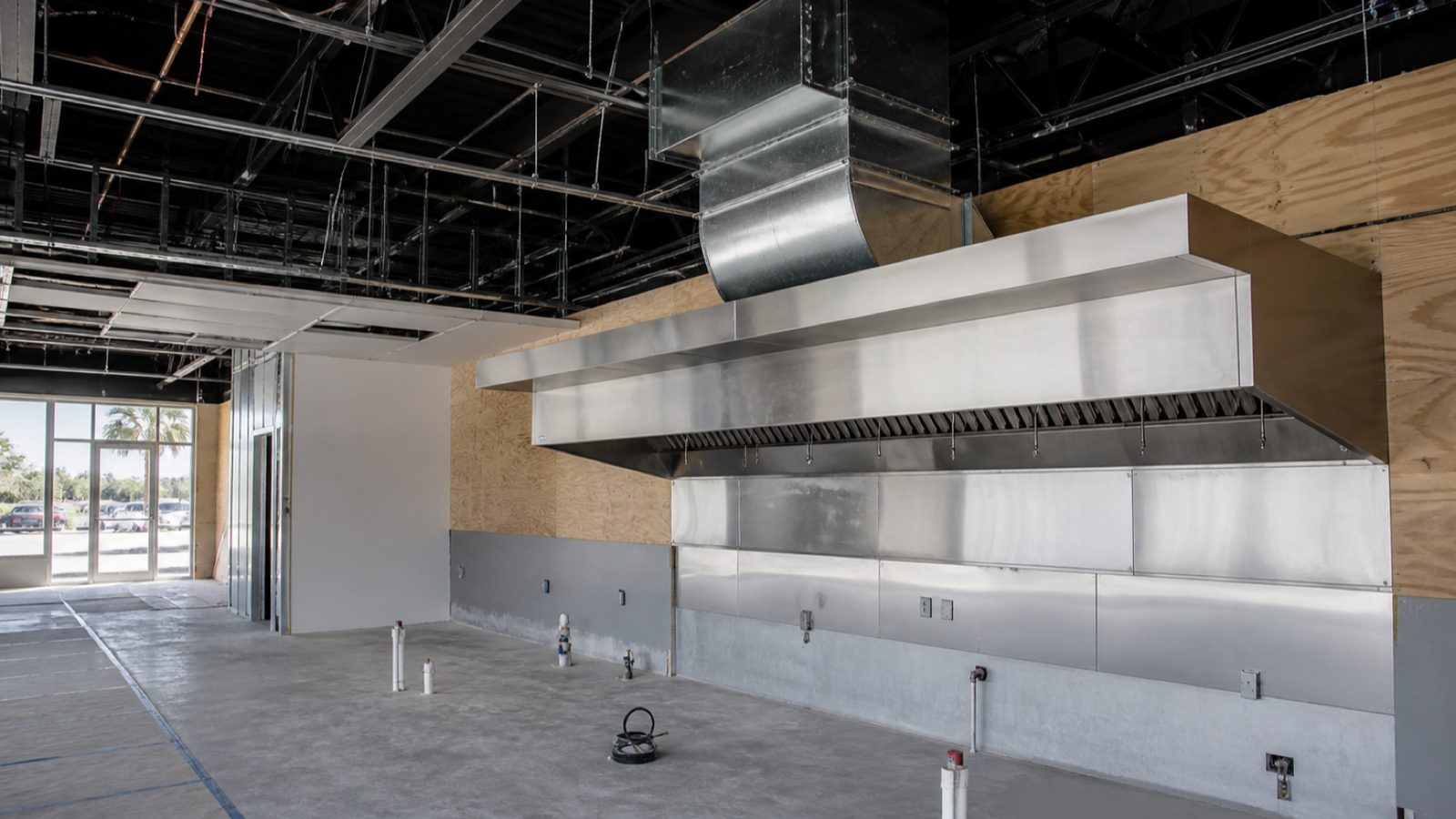 Wide stainless Type I kitchen hood with grease duct rising into an open ceiling