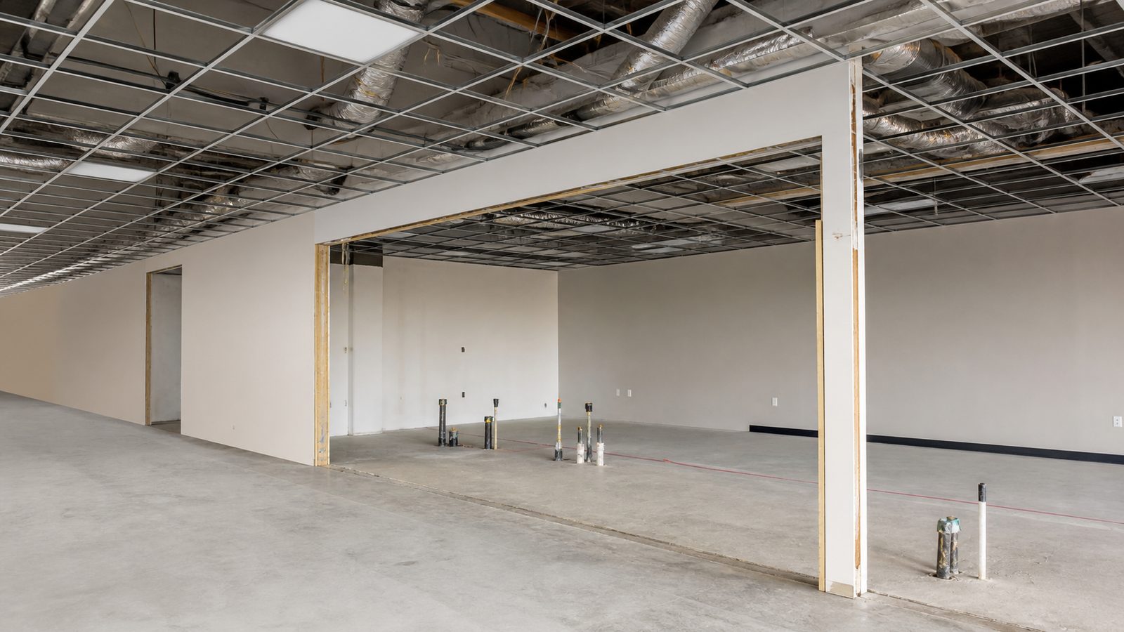 Commercial space under selective demolition with retained ceiling grid, opened partition bays, and controlled work areas