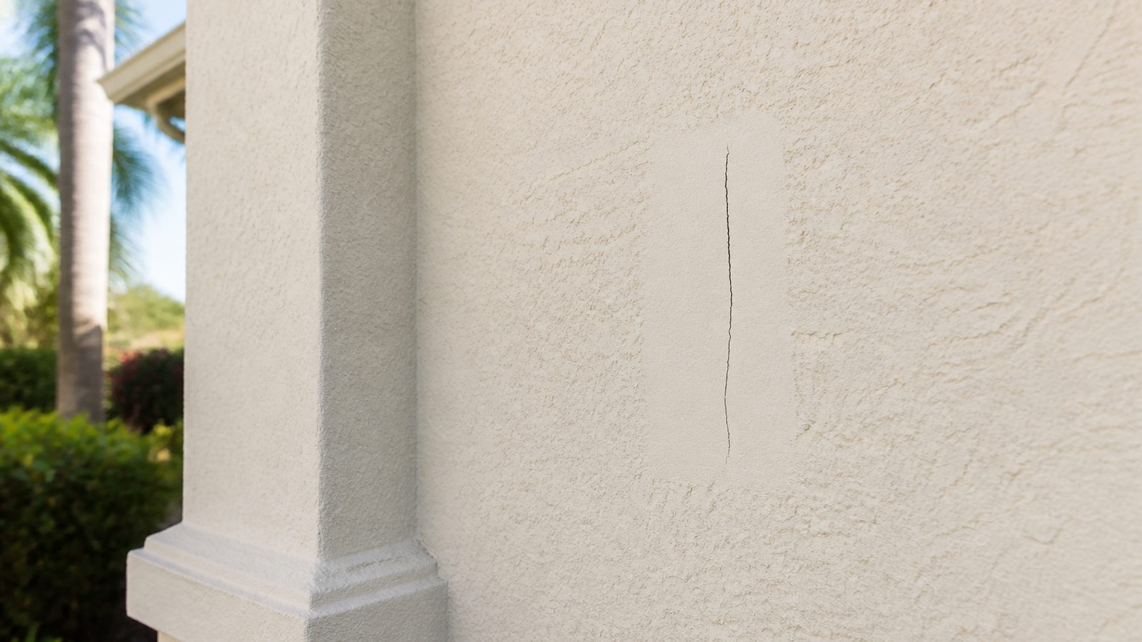 Contained dry hairline crack in an off-white stucco wall beside intact exterior trim