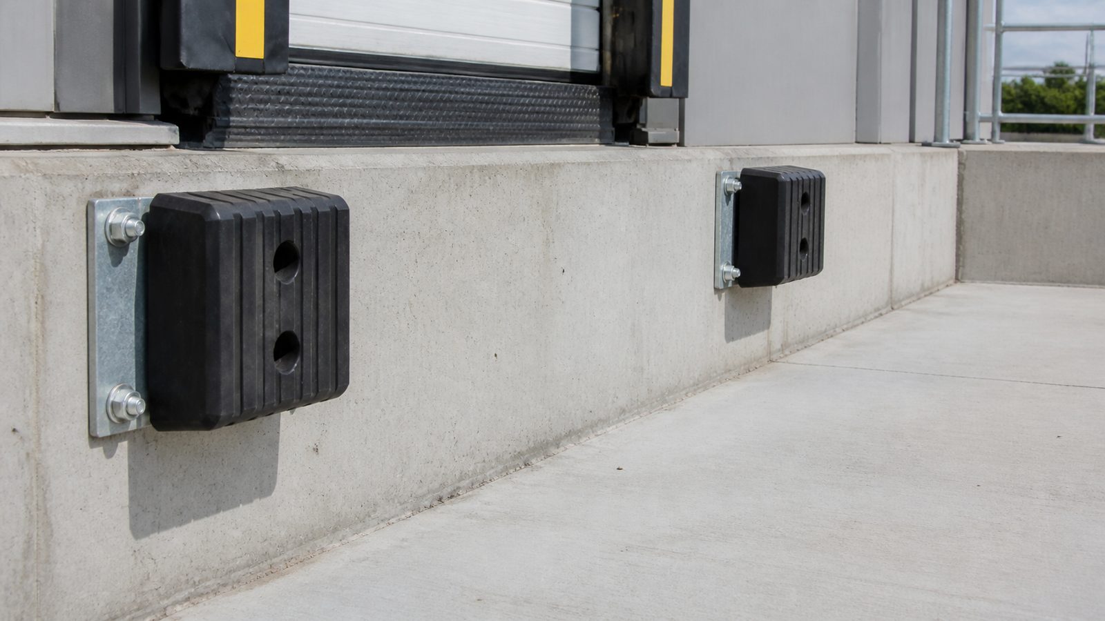 Commercial dock face with heavy rubber bumpers, galvanized plates, and visible anchor bolts at a concrete loading dock