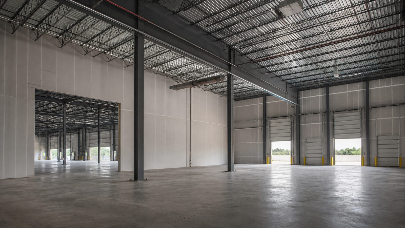 High-bay warehouse shell with exposed steel frame, concrete slab, and dock doors